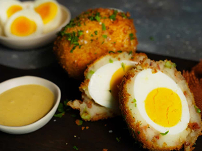 Crispy breaded egg cut in half, showing a hard-boiled egg center surrounded by seasoned mashed potato and herbs.