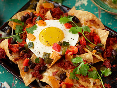 Loaded breakfast nachos topped with black beans, tomatoes, cilantro, and a fried egg.