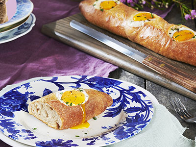 Baguette filled with a cooked egg, sliced and served on a blue floral plate.